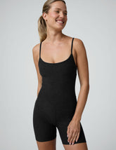 woman wearing a black biker bodysuit and sneakers on a plain background.